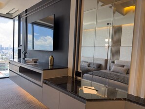 A modern hotel room with a large window, a flat-screen TV, a sofa, and a mirror reflecting the room. - SM LIVIN  STREET MALL (Heroica Puebla de Zaragoza)