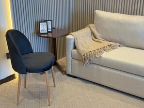 A room with a dark-colored chair, a light-colored sofa, a small round table with two framed pictures, and a textured wall.