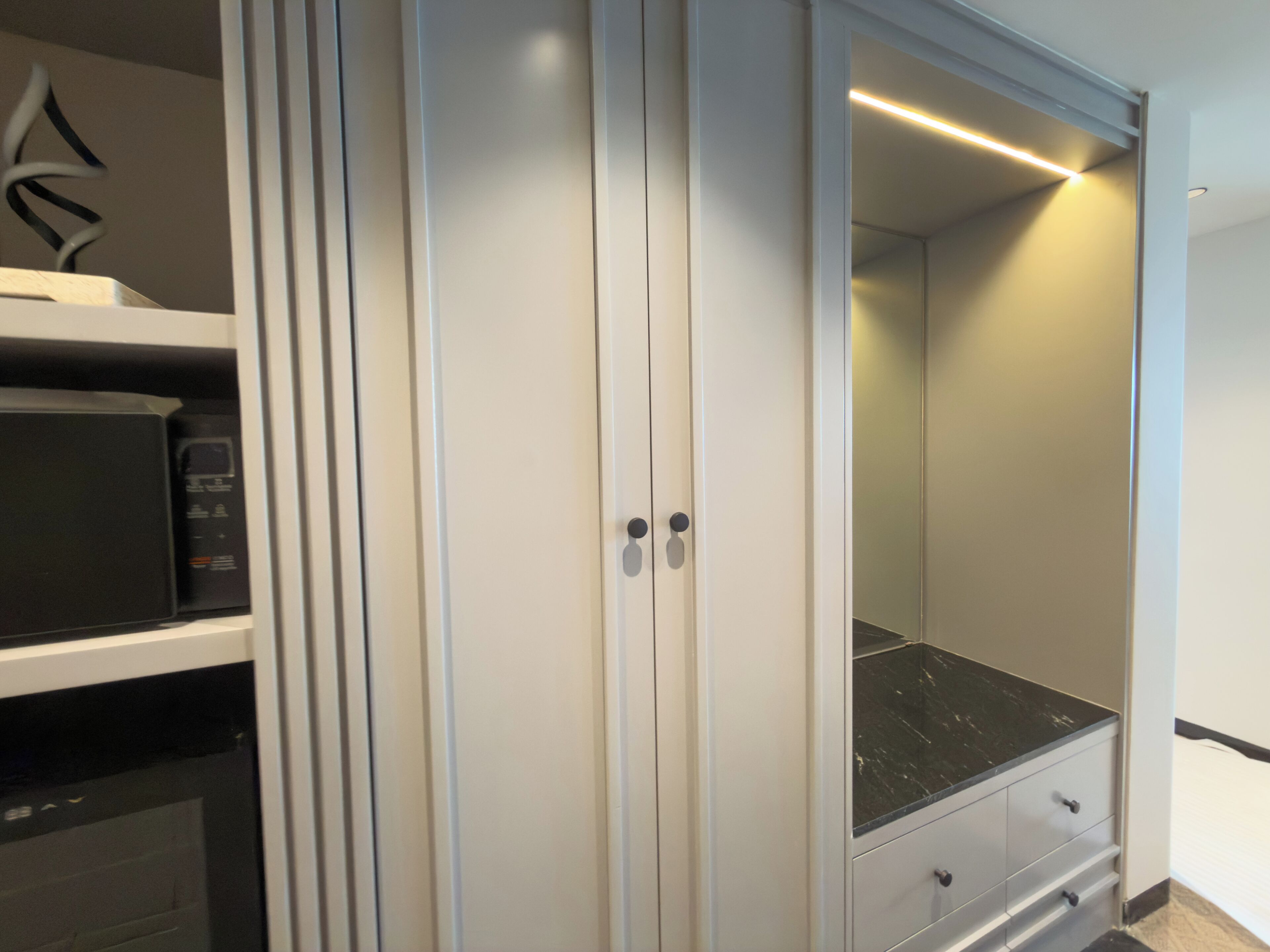A modern closet with a microwave, a black countertop, and a sliding door.