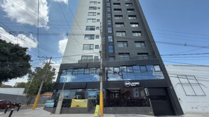 Un edificio de gran altura con varios pisos, una tienda con un cartel que dice 'SM LIVING VENTAS' y un letrero amarillo que indica servicio de valet.