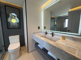 Un baño moderno con inodoro, lavamanos y encimera de mármol, y un espejo grande.