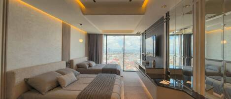 A modern hotel room with a large bed, a sofa, a TV, and a city view.