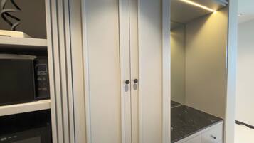 A modern closet with a microwave, a black countertop, and a mirror.