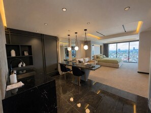 A modern hotel room with a dining area, a sofa, and a large window offering a city view.