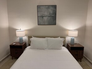 A hotel room with a bed, two bedside tables with lamps, a wall-mounted artwork, and a neutral color scheme. - Vista Cortés Ocean View | Walk to the Malecón (La Paz)