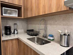 Eine Küche mit Spüle aus Edelstahl, einer Kaffeemaschine, einem Mixer, einem Geschirrgestell und einem Besteckhalter.