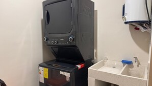 Una habitación pequeña con un electrodoméstico negro, posiblemente una lavadora, y un lavabo con un jabonera azul.