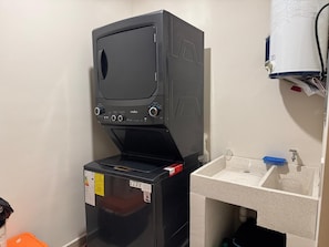 A compact room with a black appliance, possibly a washer, and a sink with a blue soap dish. - Vista Cortés Ocean View | Walk to the Malecón (La Paz)