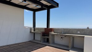 Una terraza en la azotea con piso de madera, una parrilla y una pérgola.