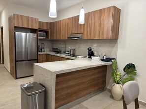 Une cuisine moderne avec des meubles en bois, des appareils en acier inoxydable, un plan de travail en granit et des luminaires suspendus.