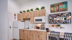 A compact kitchen with wooden cabinets, a white refrigerator, a microwave, and a coffee maker. There is a dining table with chairs and a wall-mounted picture collage. - ★The Riverwalk Getaway★ - Steps to DT - ♛Hot Tub (Fort Lauderdale)