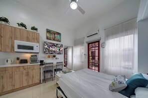 Ein kleines Zimmer mit Küchenzeile, einem Bett, einem Schreibtisch und einem fenster mit Vorhängen.