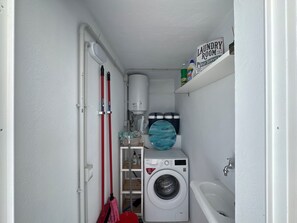 Ein kleiner Hauswirtschaftsraum mit Waschmaschine, Badewanne und Ablage für Reinigungsmittel.