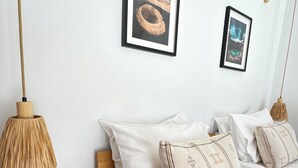 Quarto com cama de madeira, roupa de cama branca e duas molduras na parede.