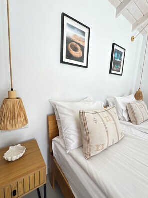 Ein Schlafzimmer mit einem hölzernen Bett, weißer Bettwäsche und zwei gerahmten Bildern an der Wand.