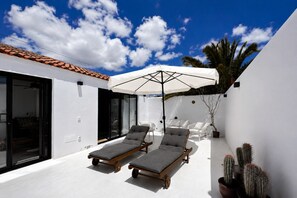 Eine moderne Terrassenanlage mit zwei Liegestühlen, einem großen Sonnenschirm und Kakteen in Töpfen.