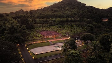 A resort with a large pool, a covered area, and a view of a lush forested hill.