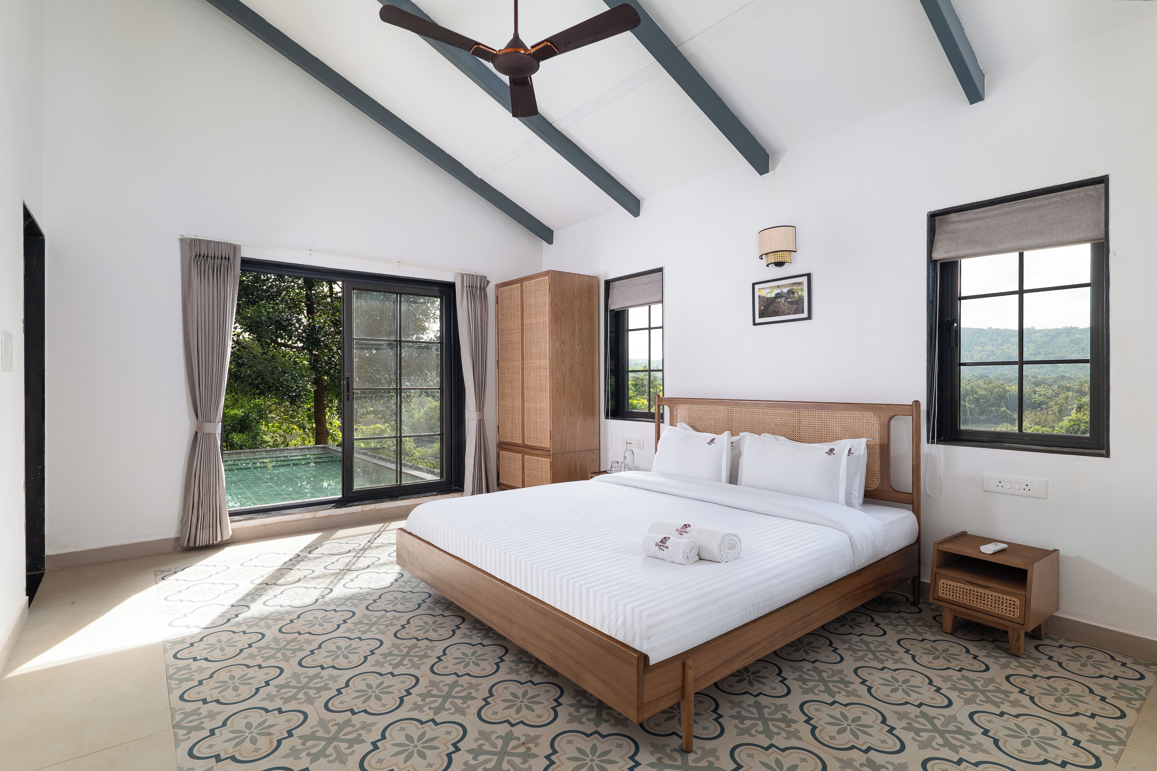 A bedroom with a large bed, a ceiling fan, and a view of greenery outside.