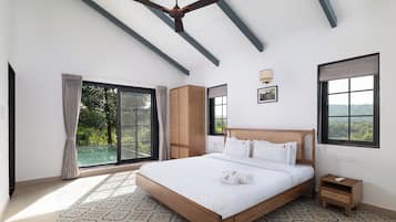 A bedroom with a large bed, a ceiling fan, and a view of greenery outside.