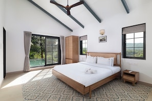 A bedroom with a large bed, a ceiling fan, and a view of greenery outside.