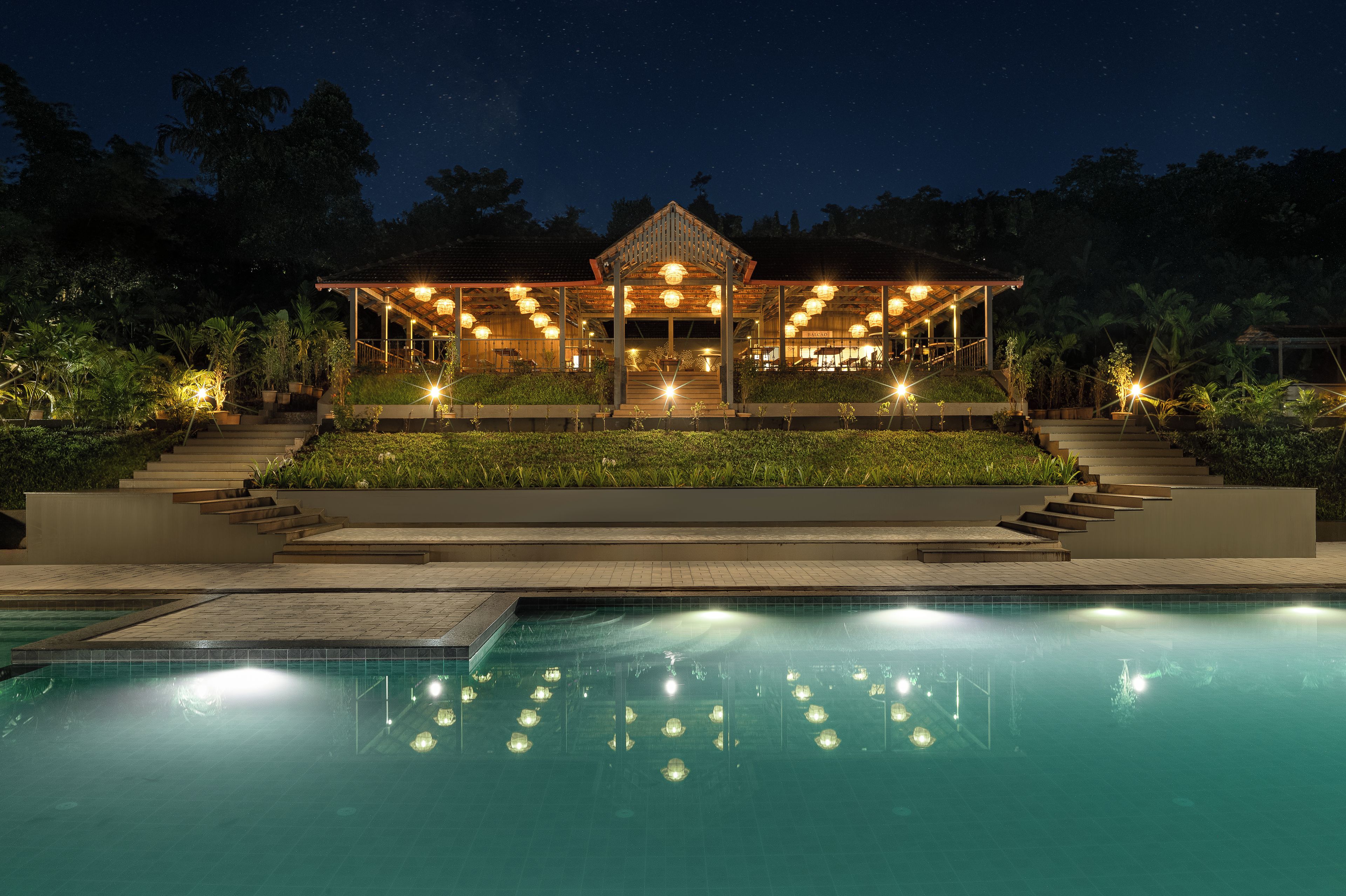 Une vue nocturne d’un complexe hôtelier avec une piscine, un espace extérieur couvert aménagé avec des sièges et une entrée bien éclairée.