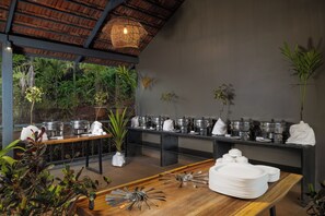 A buffet setup with multiple serving stations, a variety of dishes, and a natural backdrop.