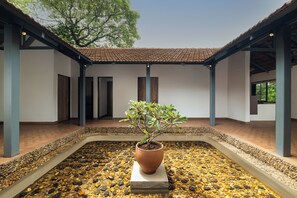 A courtyard with a central potted plant, surrounded by a pebble-lined area and covered by a tiled roof structure.