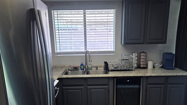 A kitchen with a stainless steel refrigerator, a sink, cabinets, and a window with blinds. - 3-bedroom house in tranquil Las Vegas with cool vibes (Las Vegas)