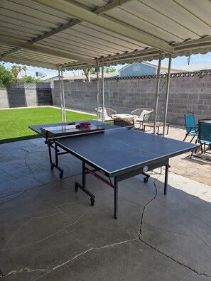 Un espacio al aire libre techado con mesa de ping pong, sillas y una mesa con asientos.