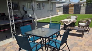 An outdoor patio area with a table and chairs, a covered seating area, and a building with a metal roof and windows. - 3-bedroom house in tranquil Las Vegas with cool vibes (Las Vegas)