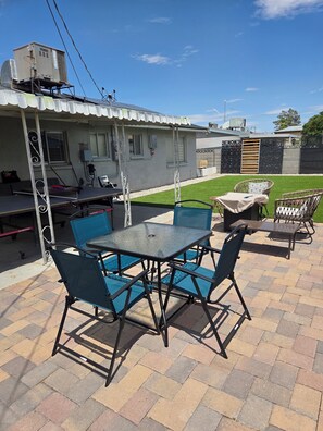 An outdoor patio area with a table and chairs, a covered seating area, and a building with a metal roof and windows. - 3-bedroom house in tranquil Las Vegas with cool vibes (Las Vegas)