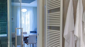 Uma casa de banho moderna com cabine de duche em vidro, um porta-toalhas branco e uma área de refeições visível, com mesa e cadeiras.