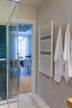 Ein modernes Badezimmer mit Duschkabine aus Glas, einem weißen Handtuchhalter und einem sichtbaren Essbereich mit Tisch und Stühlen.