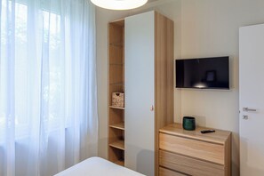 Ein Schlafzimmer mit einem Bett, einem Kleiderschrank, einem Fernseher und einem Nachttisch mit Fernbedienung.