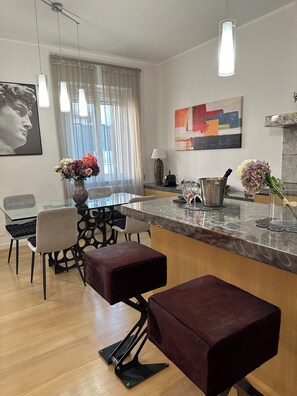 A modern kitchen with a marble countertop, pendant lighting, a dining area with a glass table, and a bar area with stools. - Bright and quiet, located between Campo de Fiori and Piazza Farnese. (Roma)