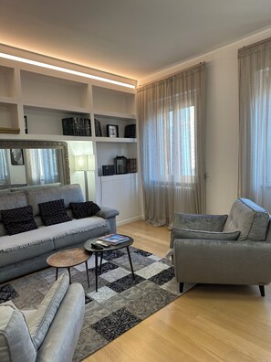 A modern living room with a grey sofa, a smaller armchair, a coffee table, and a bookshelf. - Bright and quiet, located between Campo de Fiori and Piazza Farnese. (Roma)