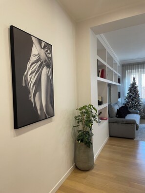 A living room with a large framed artwork, a potted plant, a bookshelf, a grey sofa, and a decorated Christmas tree. - Bright and quiet, located between Campo de Fiori and Piazza Farnese. (Roma)