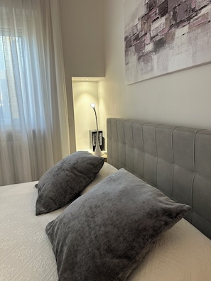 Cama bem arrumada com duas almofadas, abajur e uma obra de arte na parede.