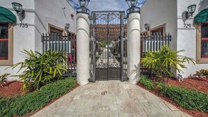 Una entrada porticada con una reja de metal, dos columnas y un camino empedrado que conduce a un edificio con los números 735 y 729 en las paredes.
