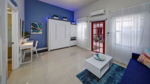Una sala de estar moderna con una pared de acento azul, muebles blancos, un ventilador de techo y una puerta con marco rojo.