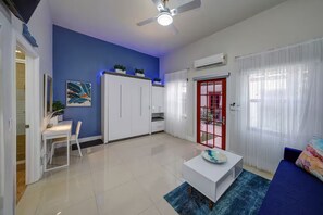A modern living room with a blue accent wall, white furniture, a ceiling fan, and a red-framed door. - Stylish Studio Oasis - Walk to Downtown - ♛Hot Tub (Fort Lauderdale)