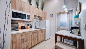 Una cocina con armarios de madera, un microondas, un refrigerador y vista al mar a través de una puerta abierta.