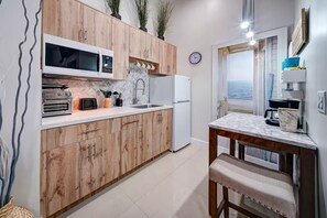 A kitchen with wooden cabinets, a microwave, a refrigerator, and a view of the sea through an open door. - Stylish Studio Oasis - Walk to Downtown - ♛Hot Tub (Fort Lauderdale)