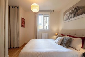 A bedroom with a bed, curtains, a window, a radiator, and a painting on the wall. - Modern Cosy 1 BDR Apt 6 min Montmartre (Paris)