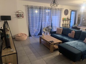 A living room with a sofa, a coffee table, a bean bag, a lamp, a wall clock, and a curtain. - 3-bedroom house with a pool, in a quiet neighborhood (Saint-Jean-de-Monts)