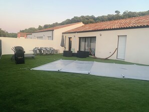 A backyard with artificial grass, a barbecue grill, outdoor furniture, and a building with a tiled roof. - 3-bedroom house with a pool, in a quiet neighborhood (Saint-Jean-de-Monts)