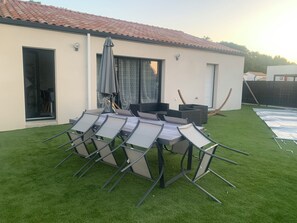 A patio with a table and chairs, a covered umbrella, and a small outdoor seating area. - 3-Bedroom House with Pool in a Quiet Neighborhood (Saint-Jean-de-Monts)