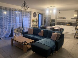 Un salon moderne comprenant un canapé, un pouf, une table basse et un coin repas avec une table et des chaises.