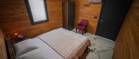 A wooden-paneled room with a bed, a chair, a wardrobe, and a door.