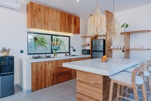 A modern kitchen with wooden cabinetry, a central island, and pendant lighting. - Brand New 2BR Villa Private Pool Rooftop (Munggu)